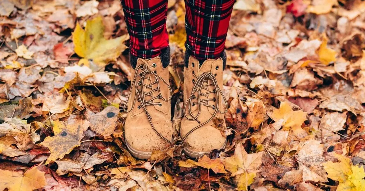 Na zasłanej jesiennymi liśćmi ziemi damskie stopy w czerwonych kraciastych rajstopach i skórzanych beżowych botkach