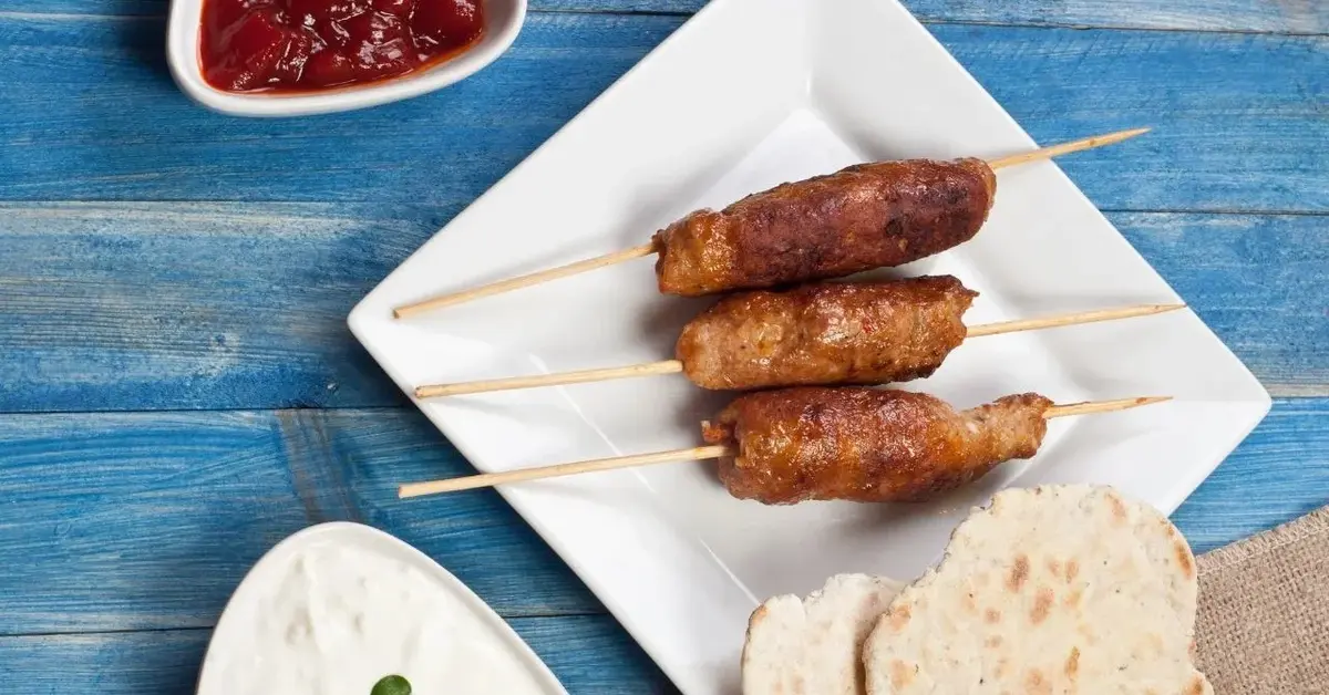 cevapcici na białym talerzu obok pieczywa pita