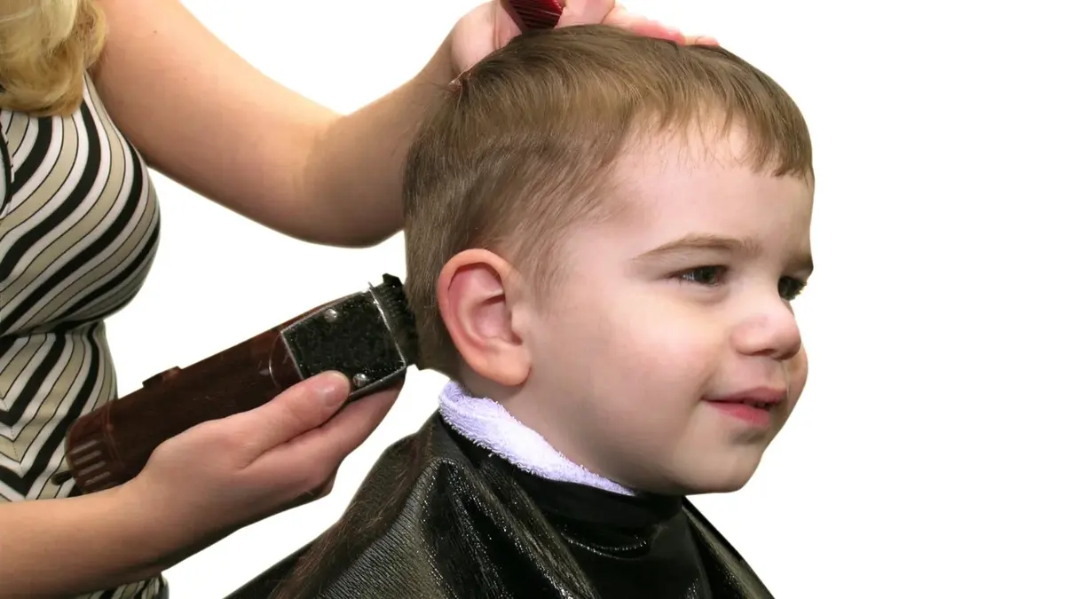 Chłopiec jest strzyżony maszynką przez fryzjera.
