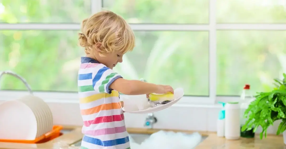 Mały chłopiec z uwagą zmywa naczynia.