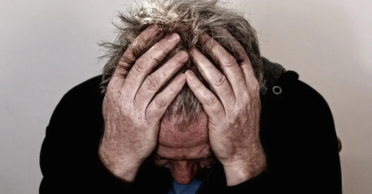 Zmęczony chorymi zatokami mężczyzna przytrzymuje dłońmi głowę kołtuniąc sobie włosy