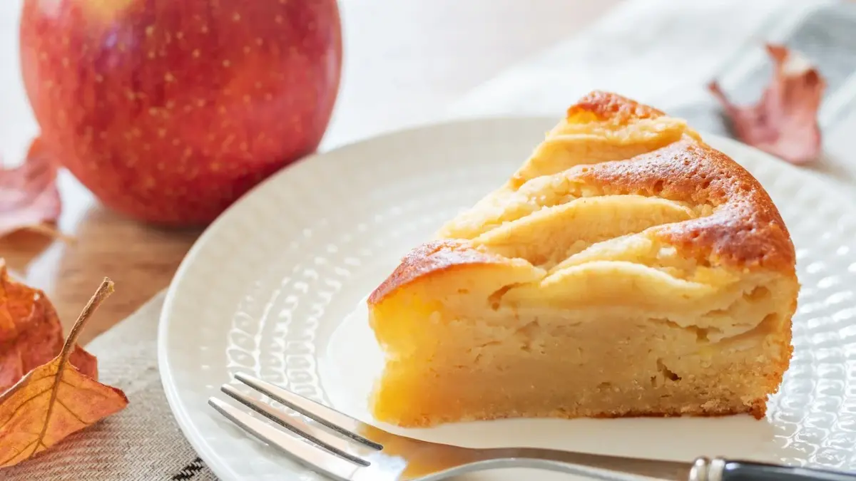 kawałek ciast na talerzu z widelcem w tle jabłko
