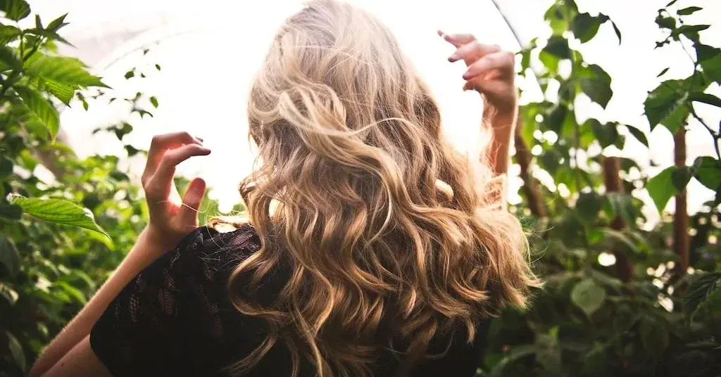 Widziana od tyłu kobieta na tle krzewów o pięknych falujących włosach bez problemu suchych włosów