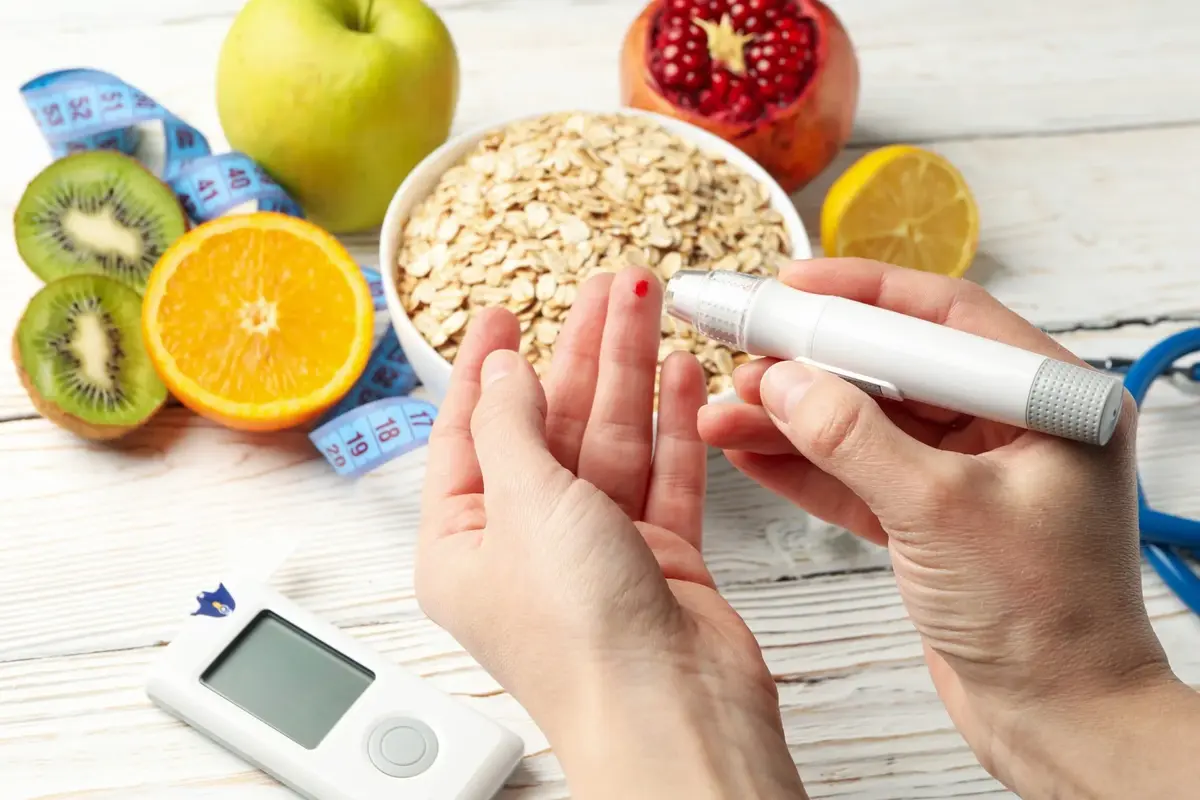 Samobadanie poziomu cukru - dłoń z kroplą krwi po nakłuciu, w tle na stole zdrowe produkty, owoce płatki