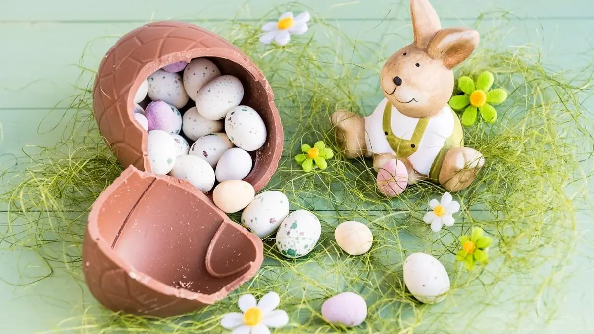 Wielkanocny zajączek siedzi koło czekoladowego jajka.