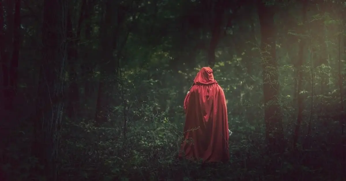 Czerwony Kapturek z baśni dla dzieci stoi w lesie.