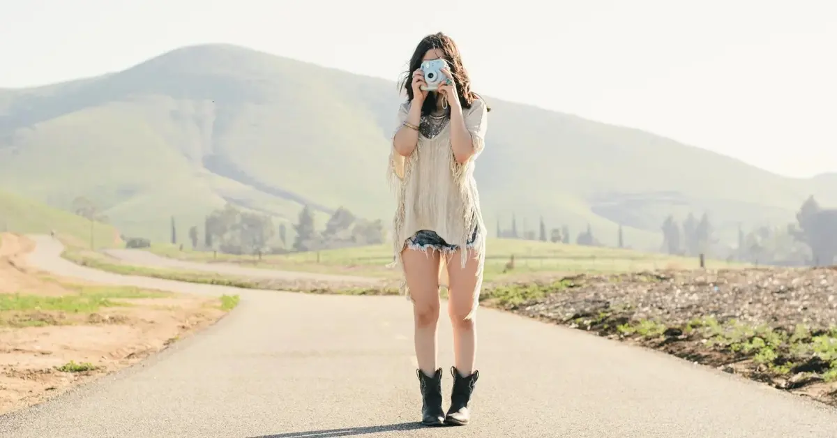 Kobieta w koszulce i dżinsowych szortach z dziurami robi zdjęcie na środku drogi z widokiem na góry