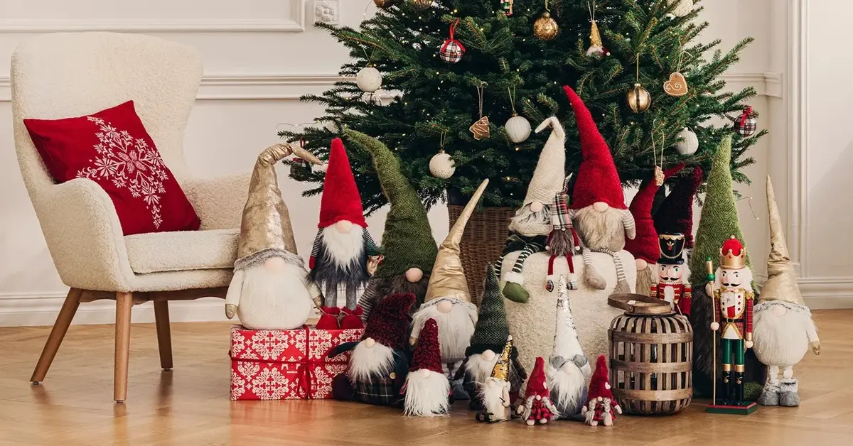 W jasnym salonie dekoracje bożonarodzeniowe, obok białego fotela ze świąteczną czerwoną poduszką choinka ze skrzatami