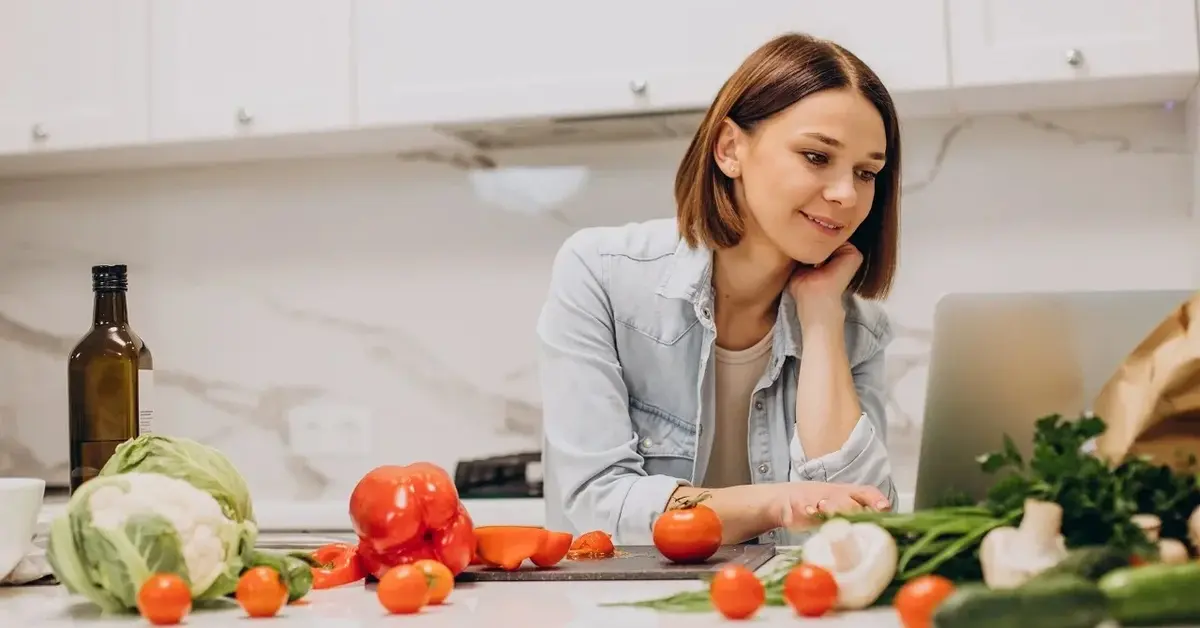 Kobieta przy wyspie w kuchni, dużo warzyw rozłożonych na blacie, sprawdza dietę online
