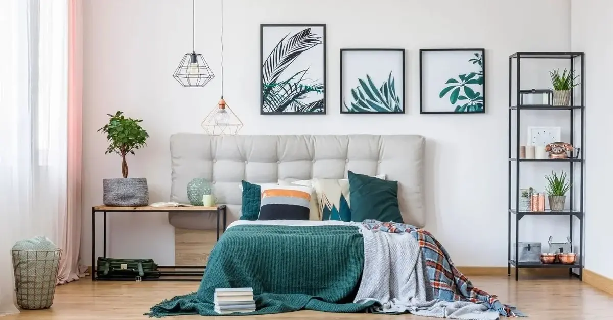 Sypialnia z łóżkiem przykrytym zieloną narzutą, z poduszkami, szarym zagłówkiem i obrazkami na ścianie