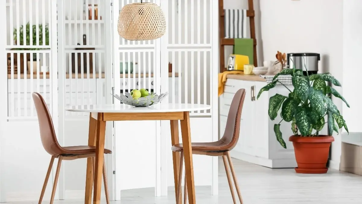 Dwa drewniane krzesła i mały stolik oddzielone od kuchni białym, drewnianym parawanem.