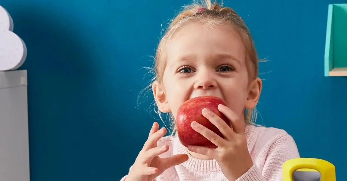 Mała dziewczynka jedząca czerwone jabłko na drugie śniadanie