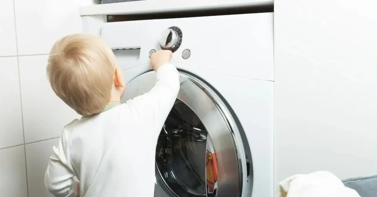 Dwuletnie dziecko bawi się pralką.