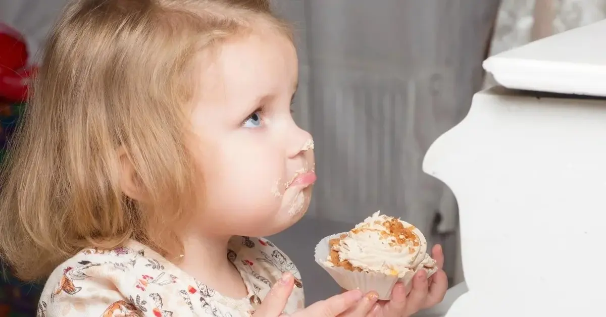 Dwuletnie dziecko ze zdegustowaną miną je ciastko.