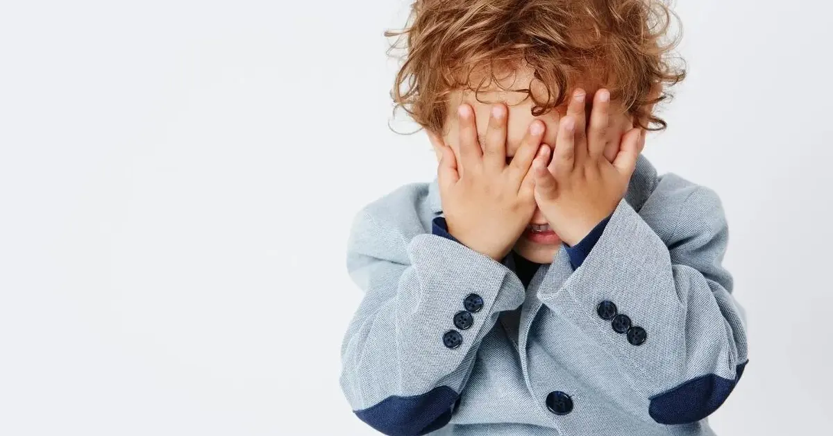 Dwulatek w marynarce zakrywa oczy.