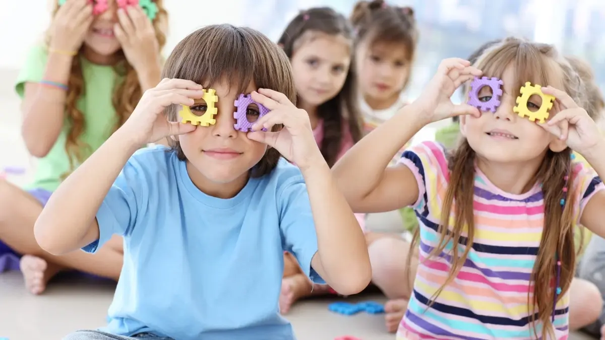 Dzieci w przedszkolu przykładają klocki z otworami do oczu.