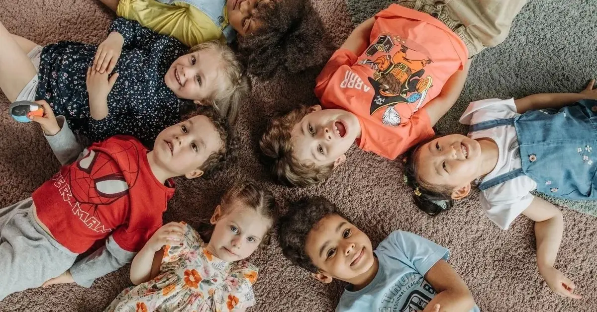 Dzieci w przedszkolu leżą w kółku i się uśmiechają.