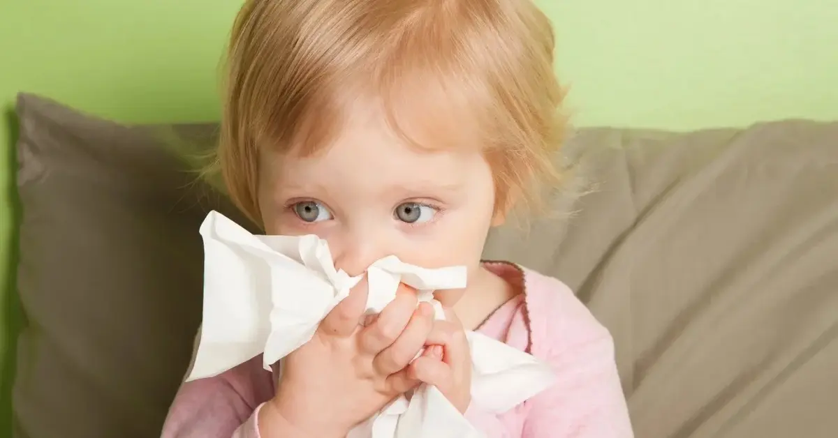 Dziecko z katarem dmucha nos w chusteczkę.