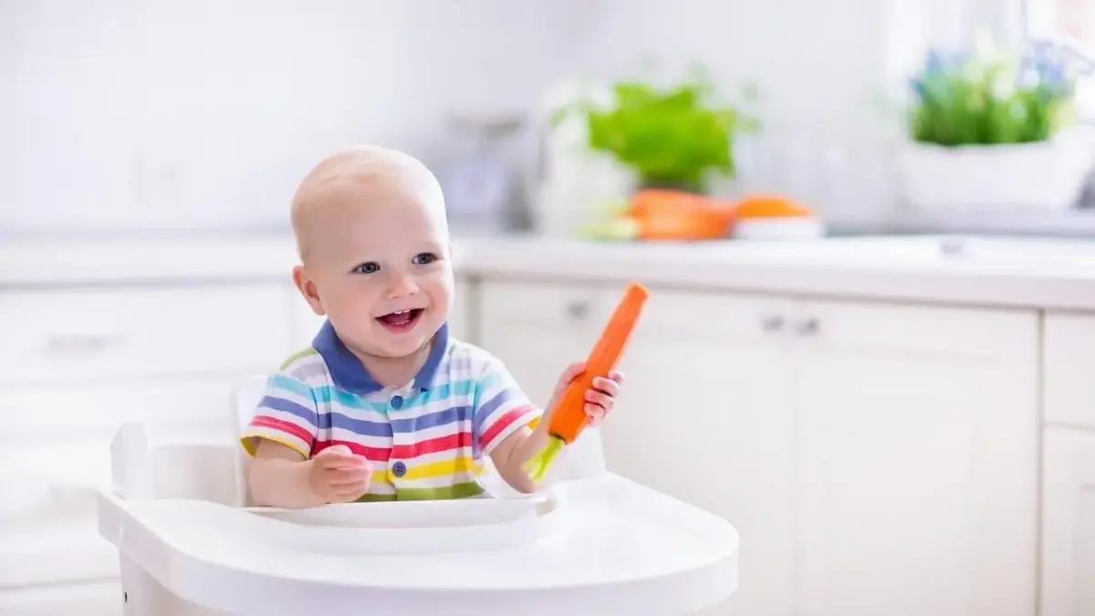 Szczęśliwe niemowlę trzyma marchewkę.