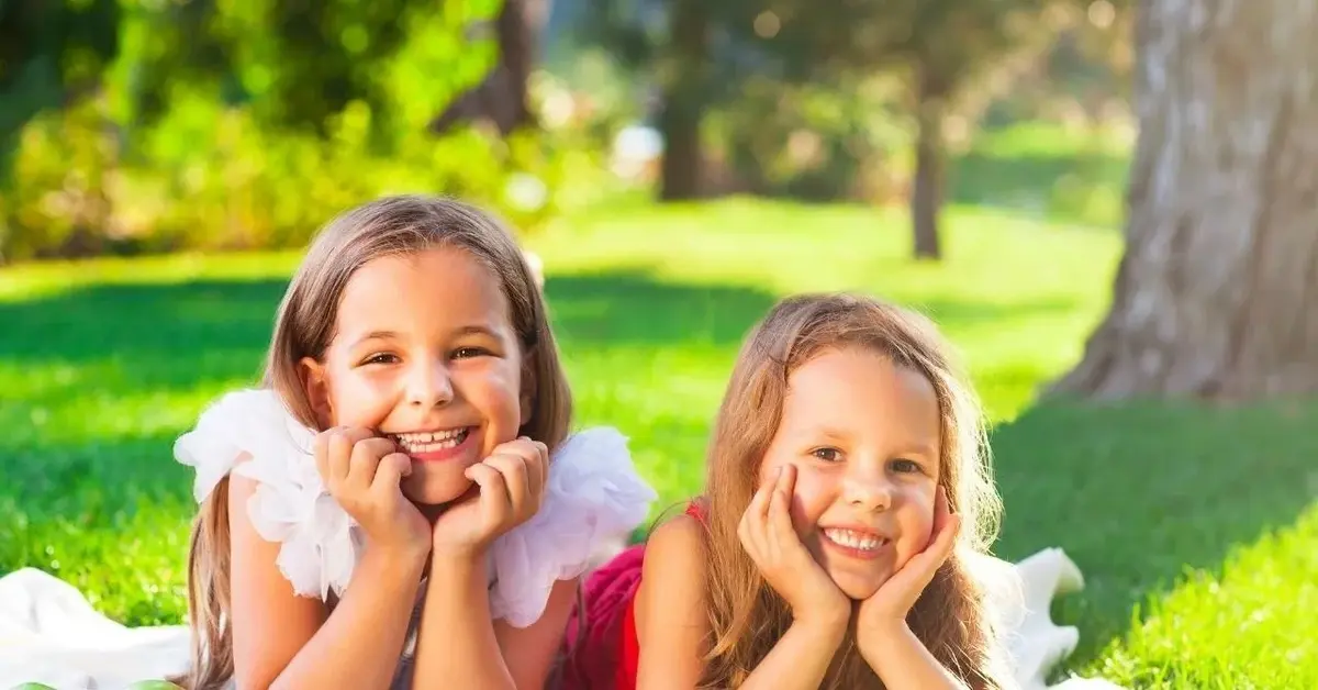 Dwie uśmiechnięte dziewczynki leżą na trawie podczas majówki.