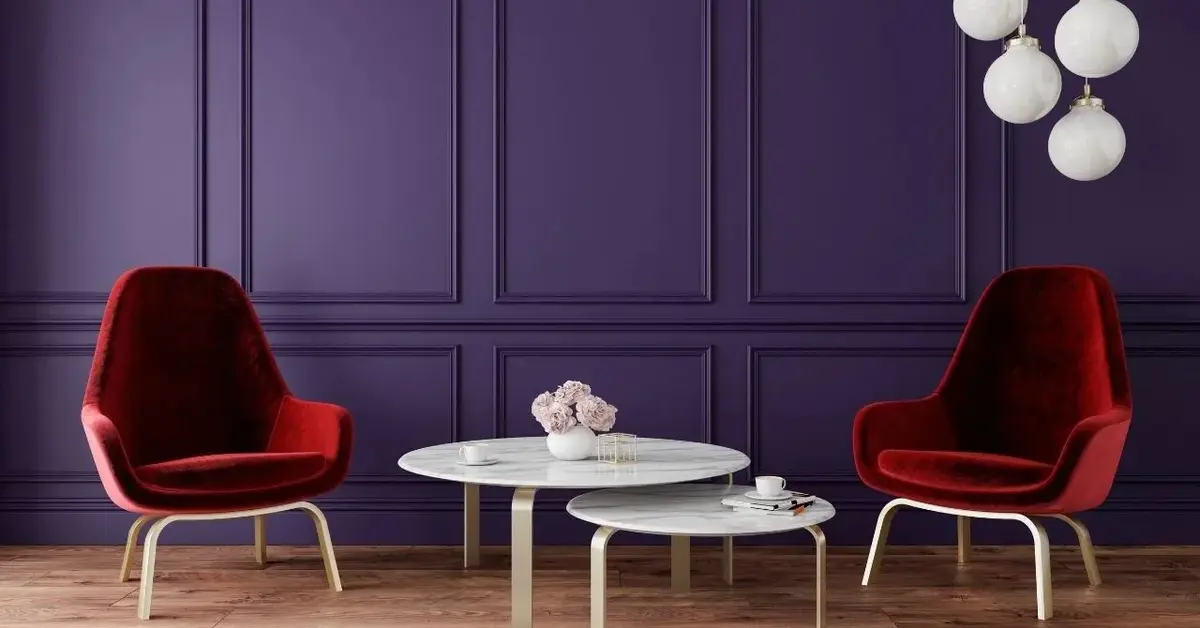 Salon z fioletową ścianą, dwoma czerwonymi fotelami i białymi stolikami kawowymi