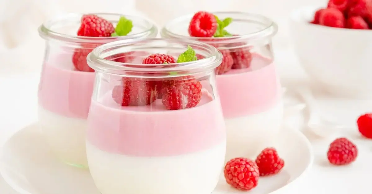 w pucharku warstwa jogurtu i galaretki jogurtowej z malinami w 3 słoiczkach z tyłu maliny w misce