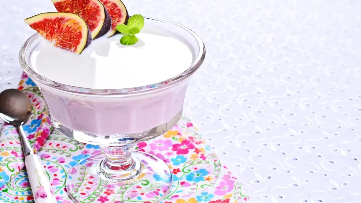 w pucharku warstwa jogurtu i galaretki jogurtowej z figą i listkiem na kolorowej serwetce z łyżką