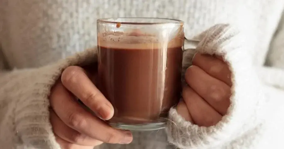 Gorąca czekolada trzymana przez osobę w swetrze.