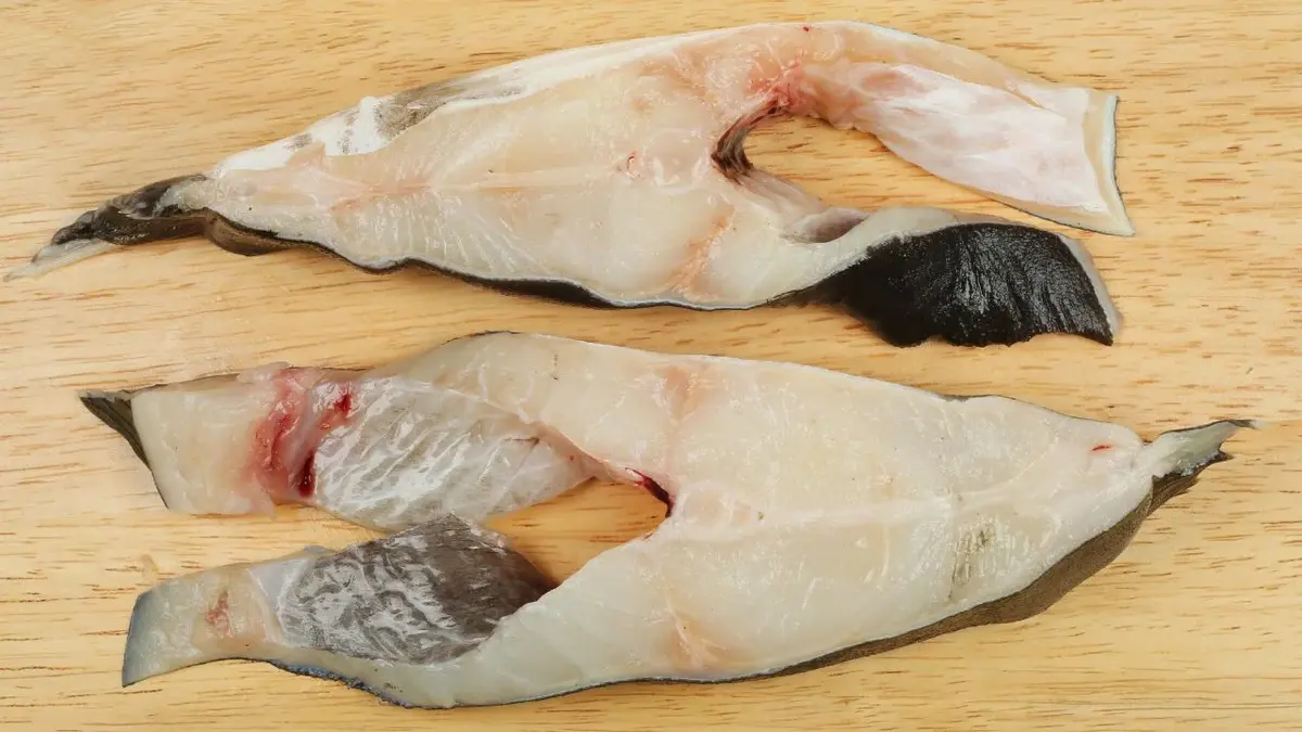 Dwa dzwonka surowego mięsa halibuta w przygotowaniu na drewnianej desce kuchennej