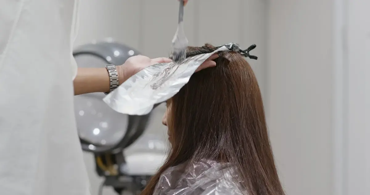 Kobieta w trakcie zabiegu farbowania włosów w zakładzie fryzjerskim