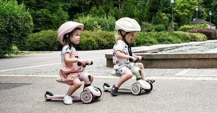 Małe dzieci na jeździkach hulajnogach w czasie spaceru w parku