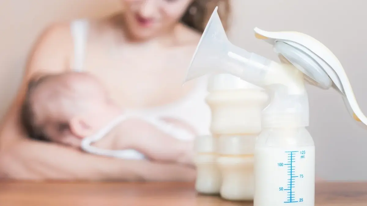 Butelki z mlekiem dla niemowlaka, w tle mama trzymająca dziecko na rękach 