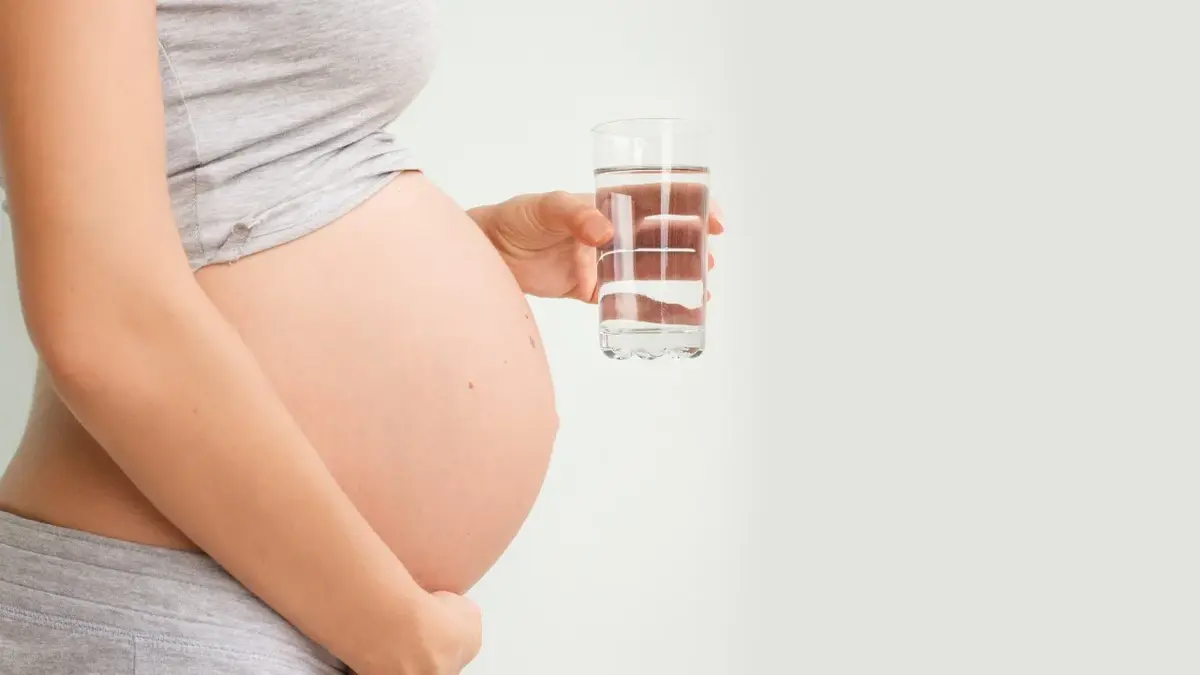 Kobieta w ciąży trzymająca szklankę wody