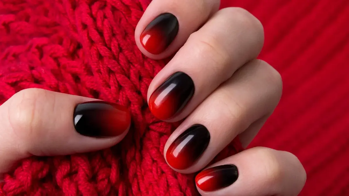 Czerwono-czarne paznokcie u ręki trzymające tkaninę dzianinowy 