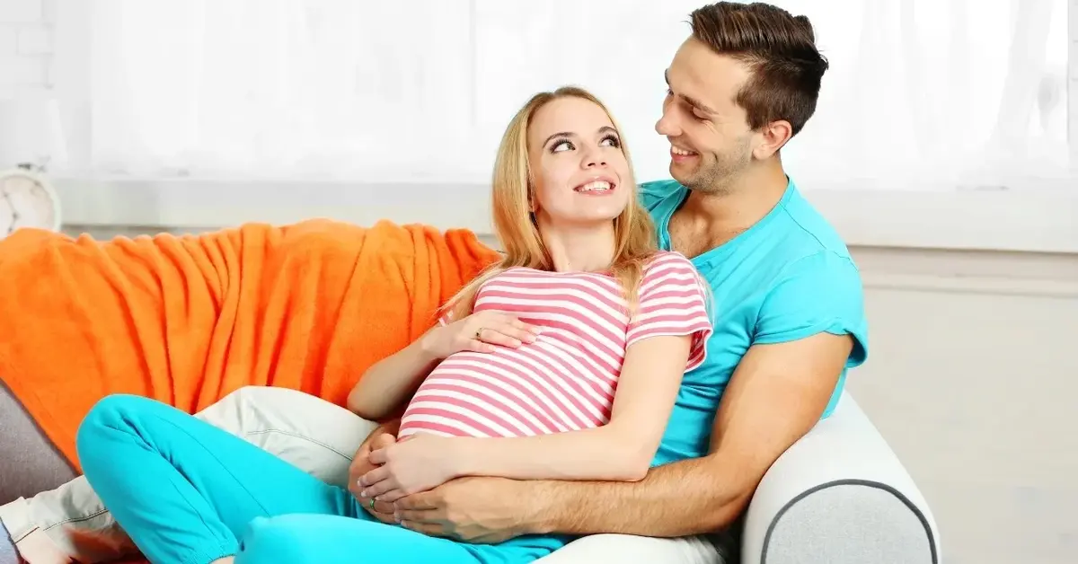 Kobieta w ciąży przytulająca się do mężczyzny na kanapie
