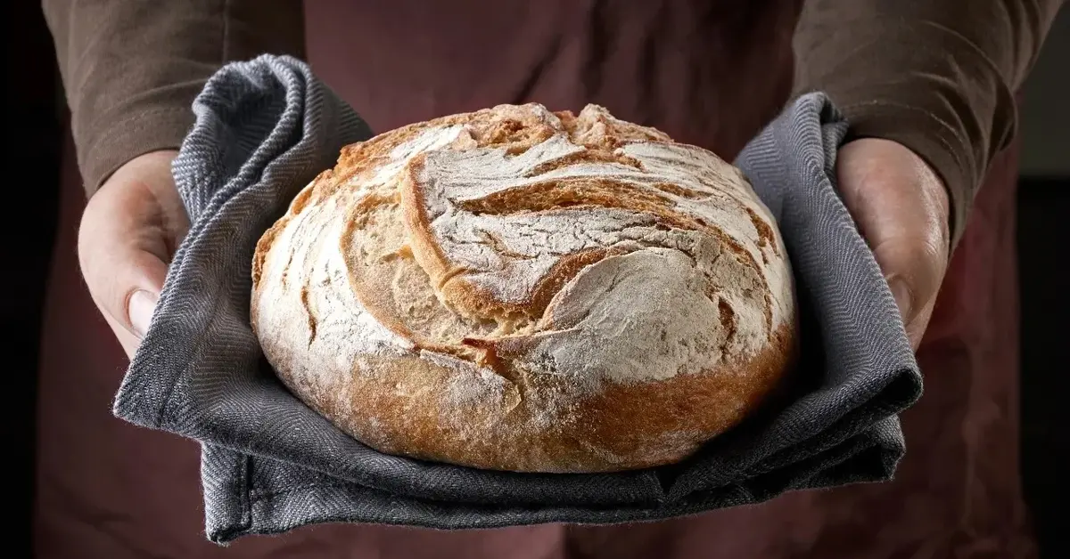 Okrągły bochenek chleba trzymany w rękach 