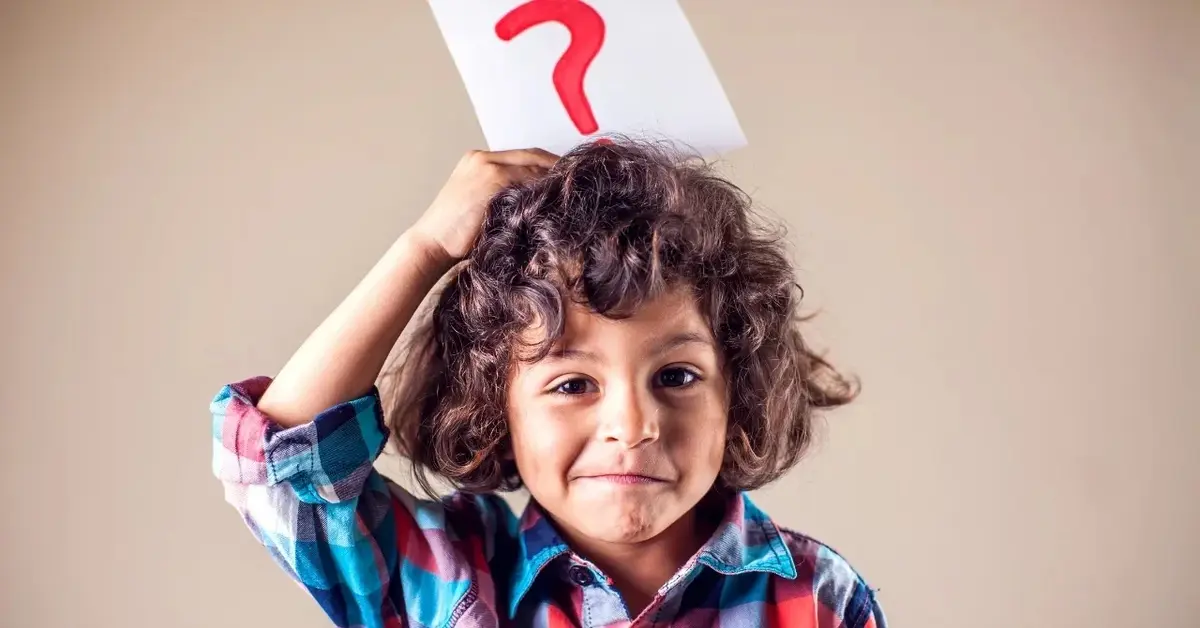 Chłopiec trzymający nad głową kartkę z narysowanym znakiem zapytanie 