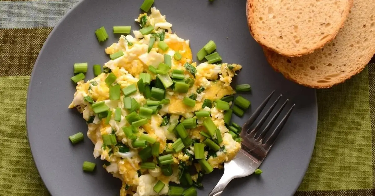 Jajecznica na talerzu posypana dużą ilością szczypiorku.