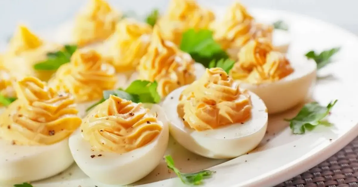 Jaja faszerowane kremem musztardowym z przepisu Ewy Wachowicz, ułożone na białym talerzu i udekorowane natką pietruszki