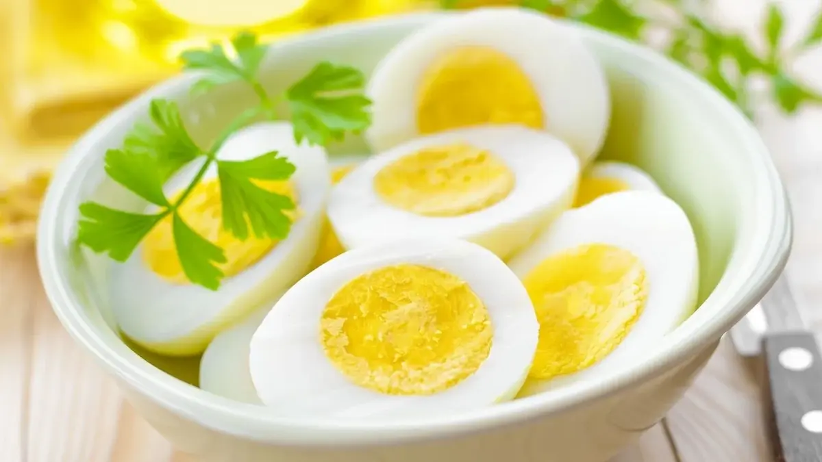 Perfekcyjnie ugotowane jajka na twardo ułożone w białej misce z listkiem pietruszki