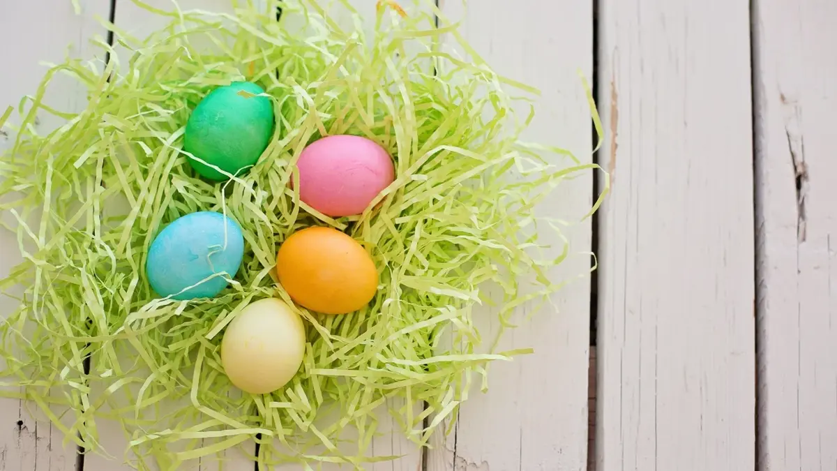 Kolorowe jajka na Wielkanoc w koszyczku z zielonego papieru.