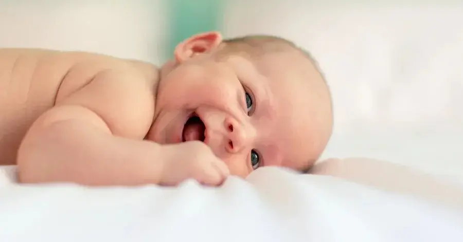 Radośnie uśmiechnięte niemowlę w czystej zadbanej pościeli dla niemowlaka