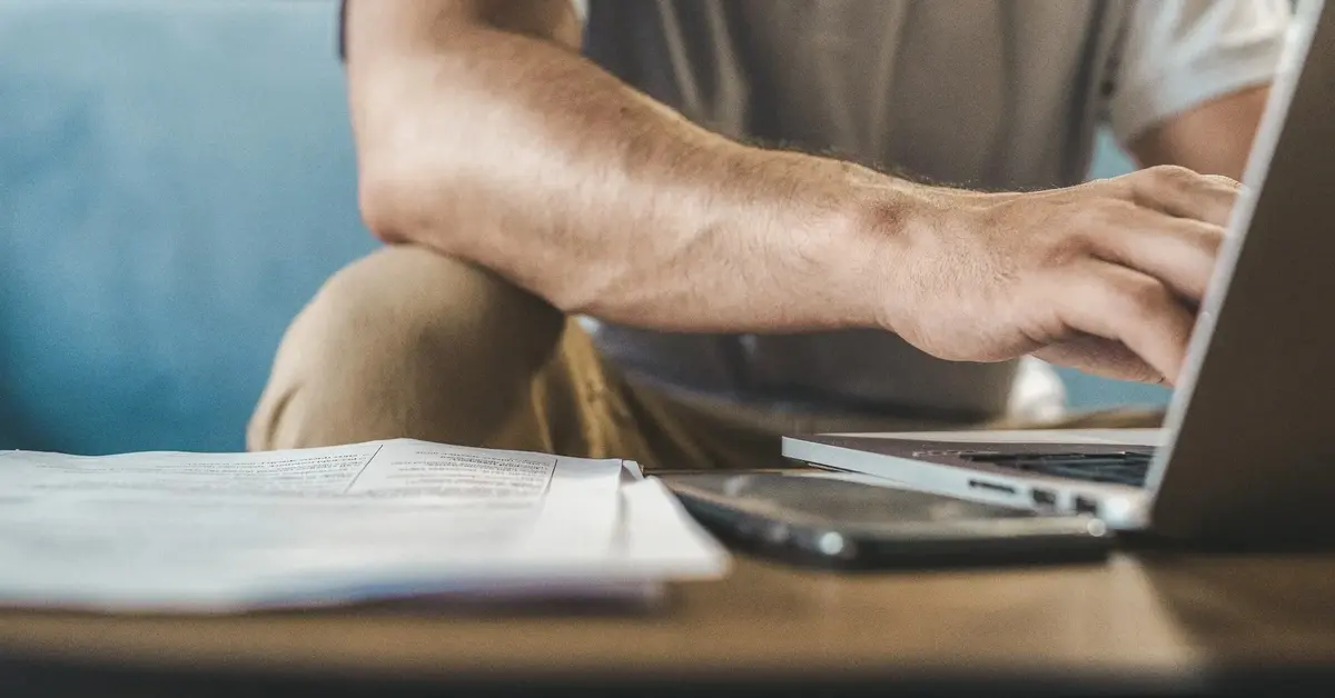 Mężczyzna w podkoszulku siedząc na kanapie sprawdza w komputerze jak przenieść się do orange