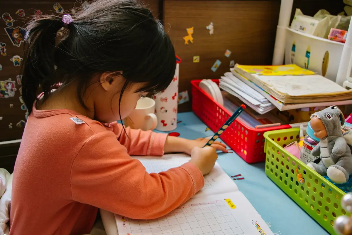 W pokoju dla przedszkolaka czarnowłosa dziewczynka rozwiązuje zadanie domowe przy biurku