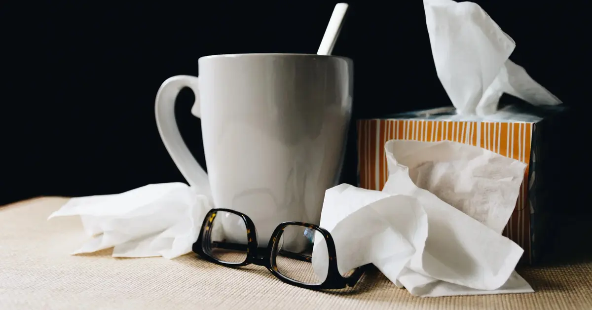 Na stole kubek z ciepłym napojem chusteczki do nosa i okulary