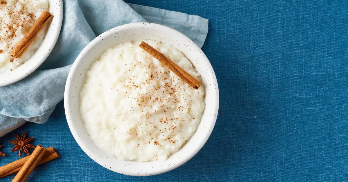 Na niebieskim obrusie biała miseczka z ugotowanym na mlu ryżem i laską cynamonu, obok jasnoniebieska ściereczka