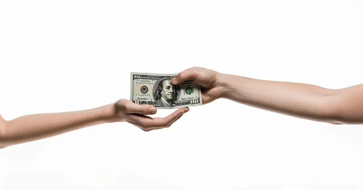 Dwie ręce podające sobie nawzajem plik pieniędzy w ramach pożyczki