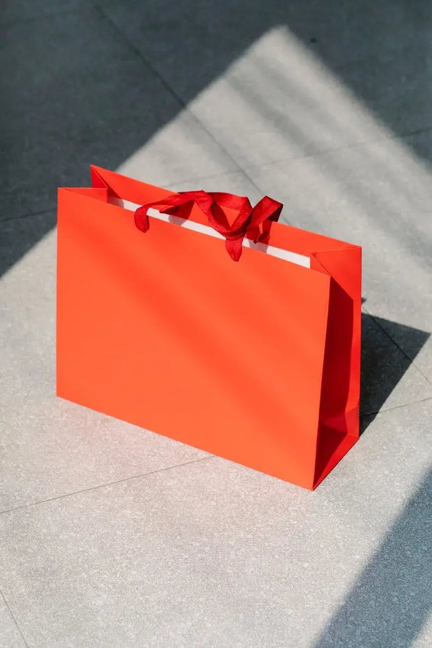 Na neutralnym tle prezent zapakowany w jaskrawo-pomarańczową torebkę prezentową