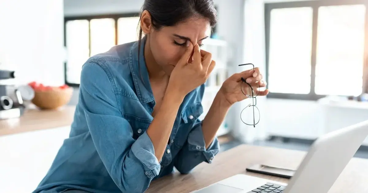 W domowym biurze przed komputerem kobieta w dżinsowej koszuli podpiera głowę dłonią w geście walki ze stresem