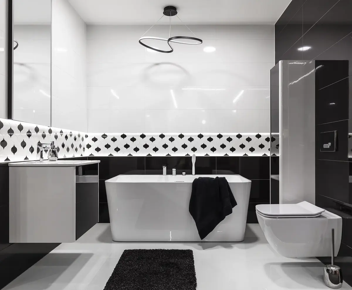 Łazienka utrzymana w bieli i czerni z wygodną wanną pośrodku oraz czarnymi elementami dekoracyjnymi